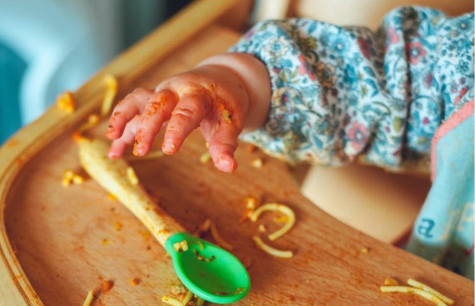 baby grabbing for spoon and eating spaghetti