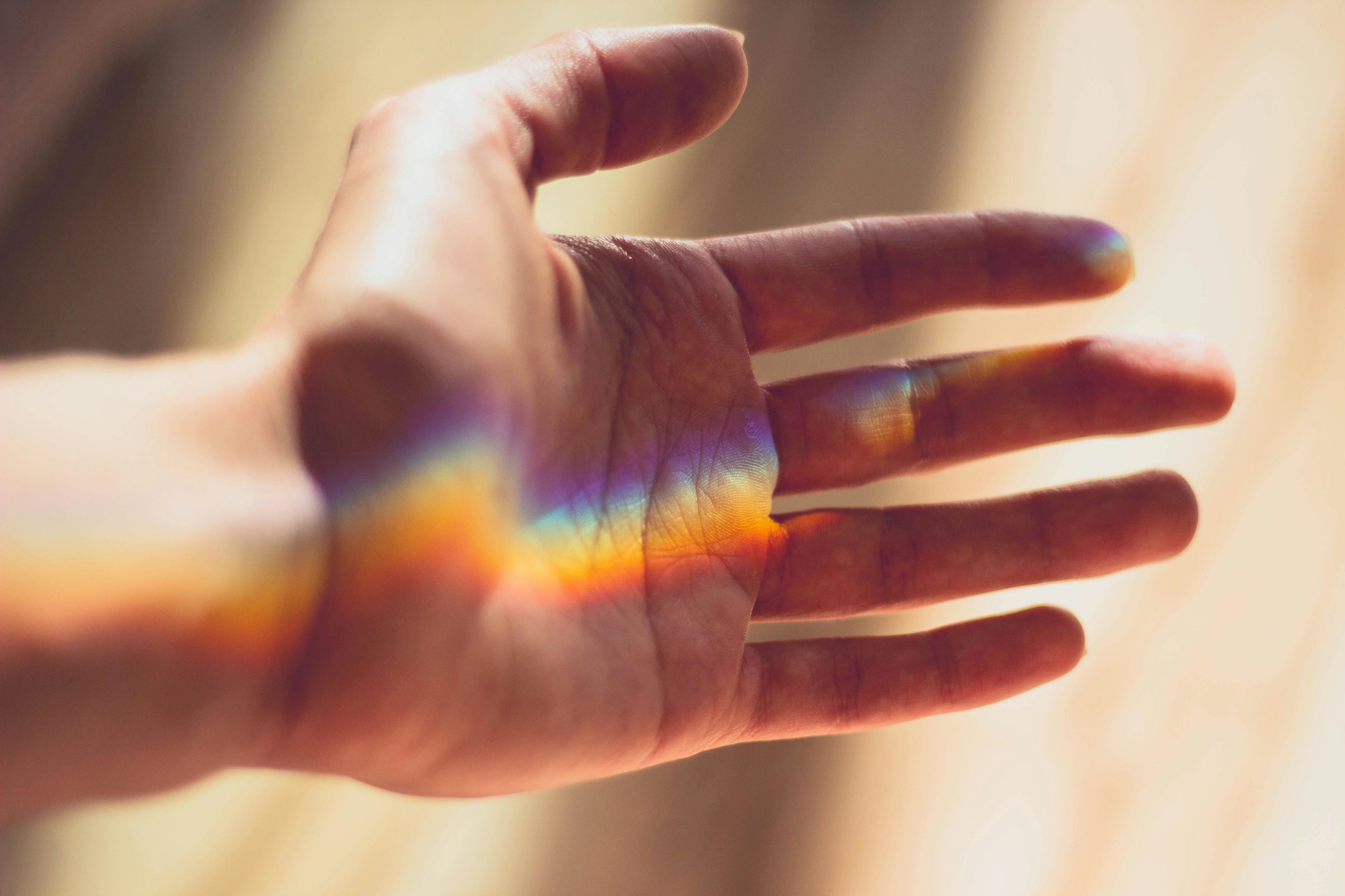 image of an open hand with a reflection of a rainbow spectrum 