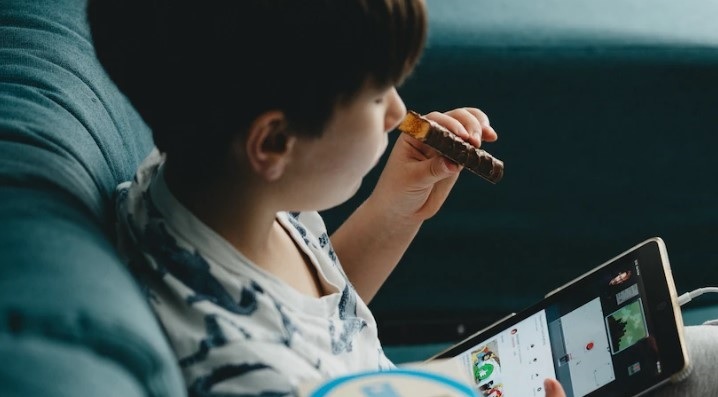 Child with tablet computer eating chocolate bar